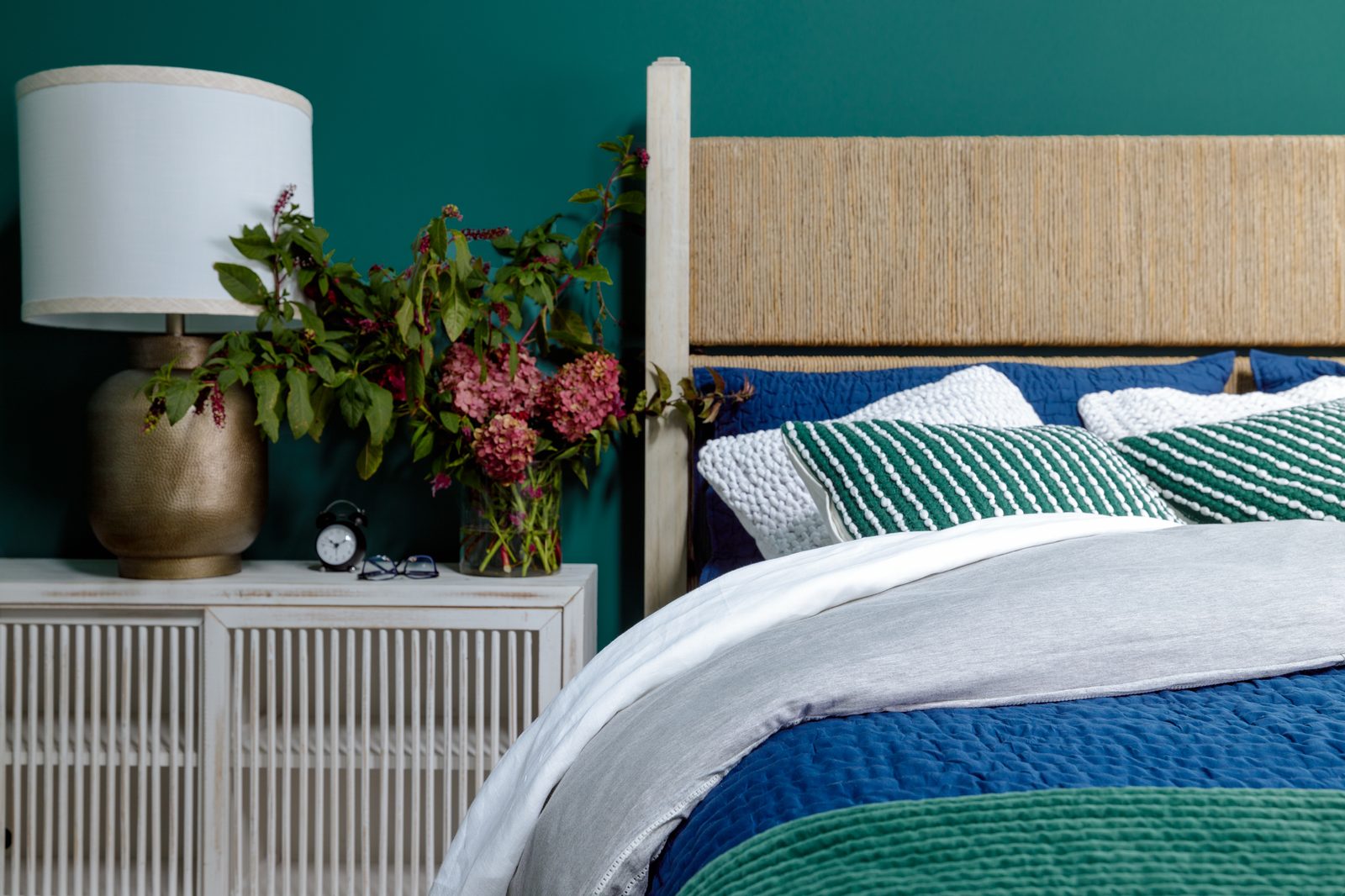 Interior design photography detail vignette of a styled bedroom nightstand with brass lamp, textured bedding, and teal accent wall